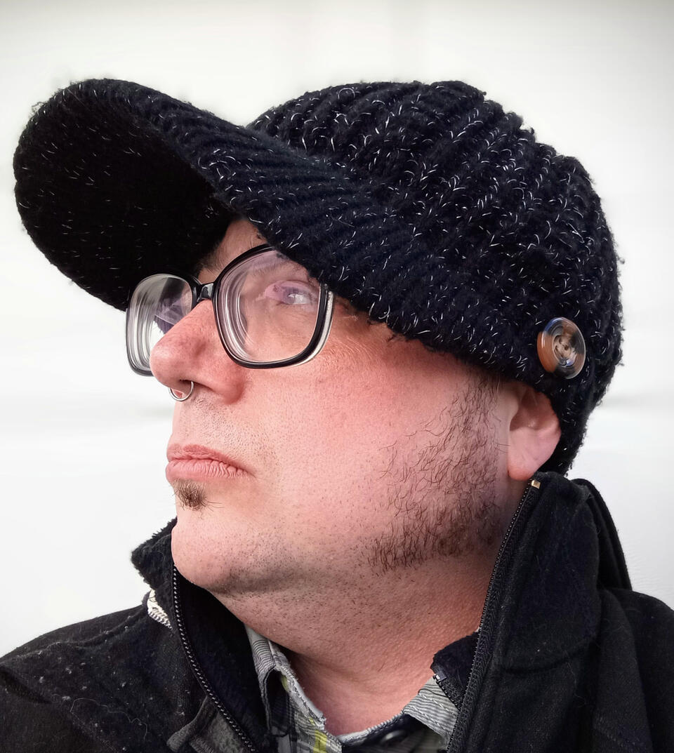 A white man with black knit cap, black glasses, and muttonchops.